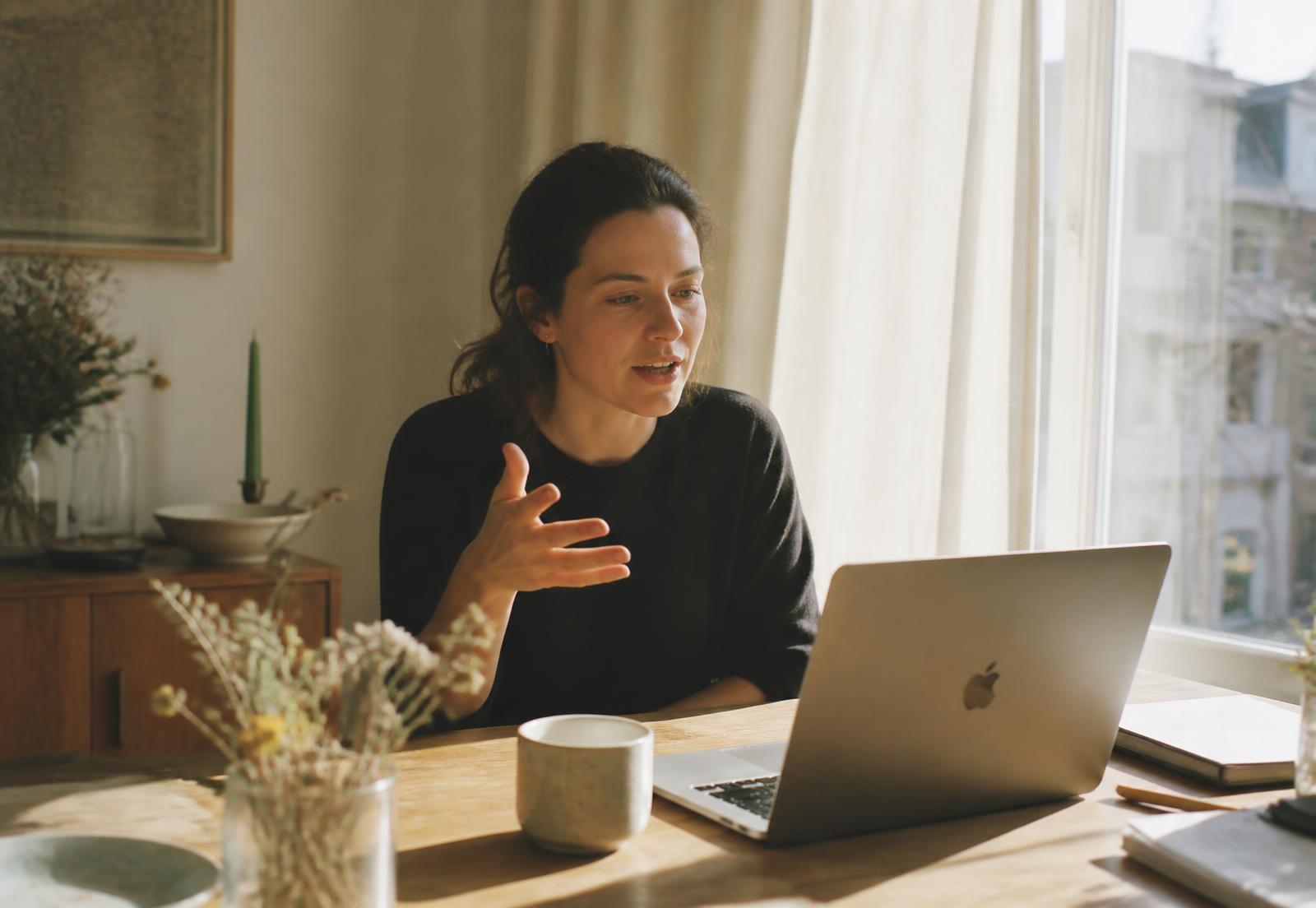 A woman speaking to her laptop at a sunlit desk while Murmur AI types for her